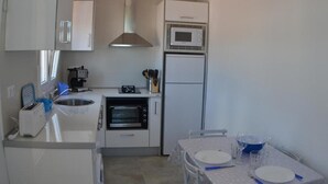 A compact kitchen with a microwave, oven, and toaster. There is a dining table with plates and glasses. - Country House 'Daniela 2' with Sea View, Wi-Fi and Air Conditioning (El Pozo de los Frailes)