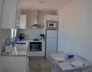 A compact kitchen with a microwave, oven, and toaster. There is a dining table with plates and glasses. - Country House 'Daniela 2' with Sea View, Wi-Fi and Air Conditioning (El Pozo de los Frailes)