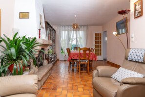 Una sala de estar con sofá, una mesa de comedor con sillas, chimenea y un ventanal con cortinas.