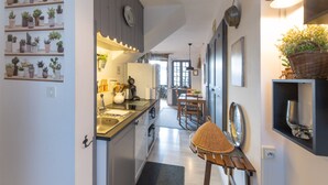 A kitchen with a clock, shelves with plants, a dining area with chairs, and a basket on a table. - Cosy Duplex Apartment - Ardèche Riverside with Private Terrace, Balcony & Wi-Fi (Lanas)