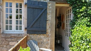 A stone building with a wooden door, a window with shutters, and a table with chairs outside. - Cosy Duplex Apartment - Ardèche Riverside with Private Terrace, Balcony & Wi-Fi (Lanas)