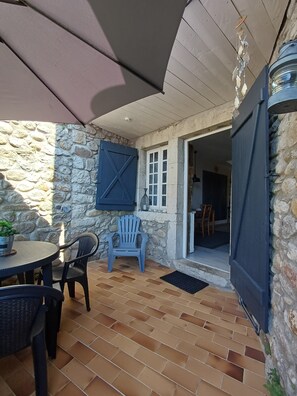 A patio area with a stone wall, a blue chair, a table, and a blue umbrella.