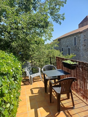 A patio with a table and chairs, surrounded by greenery and a stone building. - Cosy Duplex Apartment - Ardèche Riverside with Private Terrace, Balcony & Wi-Fi (Lanas)