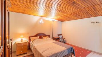 Una camera da letto con soffitto in legno, un letto, un comodino, una lampada, una sedia e un tappeto rosso.