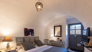 Une chambre à coucher comprenant un lit, une table de chevet, une lampe, une chaise, une commode, un miroir et une porte avec une fenêtre.