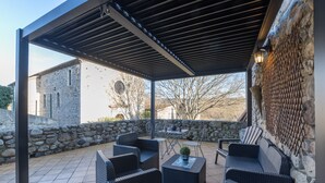 Une terrasse extérieure avec des meubles en osier, un mur en pierre et une vue sur un bâtiment historique.