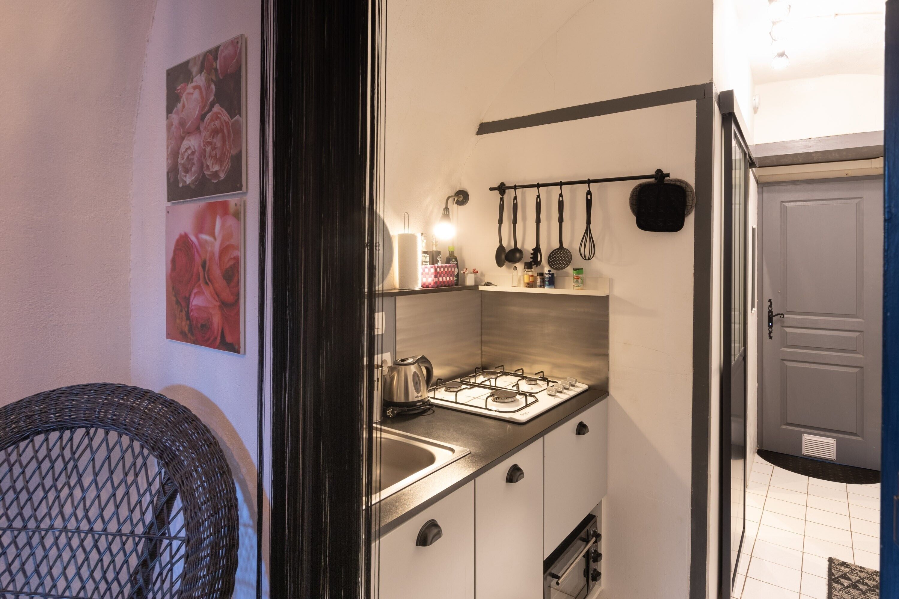 Une cuisine compacte équipée d’une cuisinière à gaz, d’un évier et d’ustensiles suspendus.