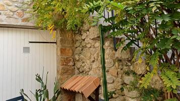 A stone wall with a cactus and potted plants, a metal bench, and a table with a striped tablecloth.