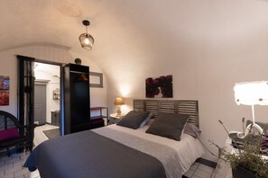 A bedroom with a bed, bedside table, lamp, and a potted plant.