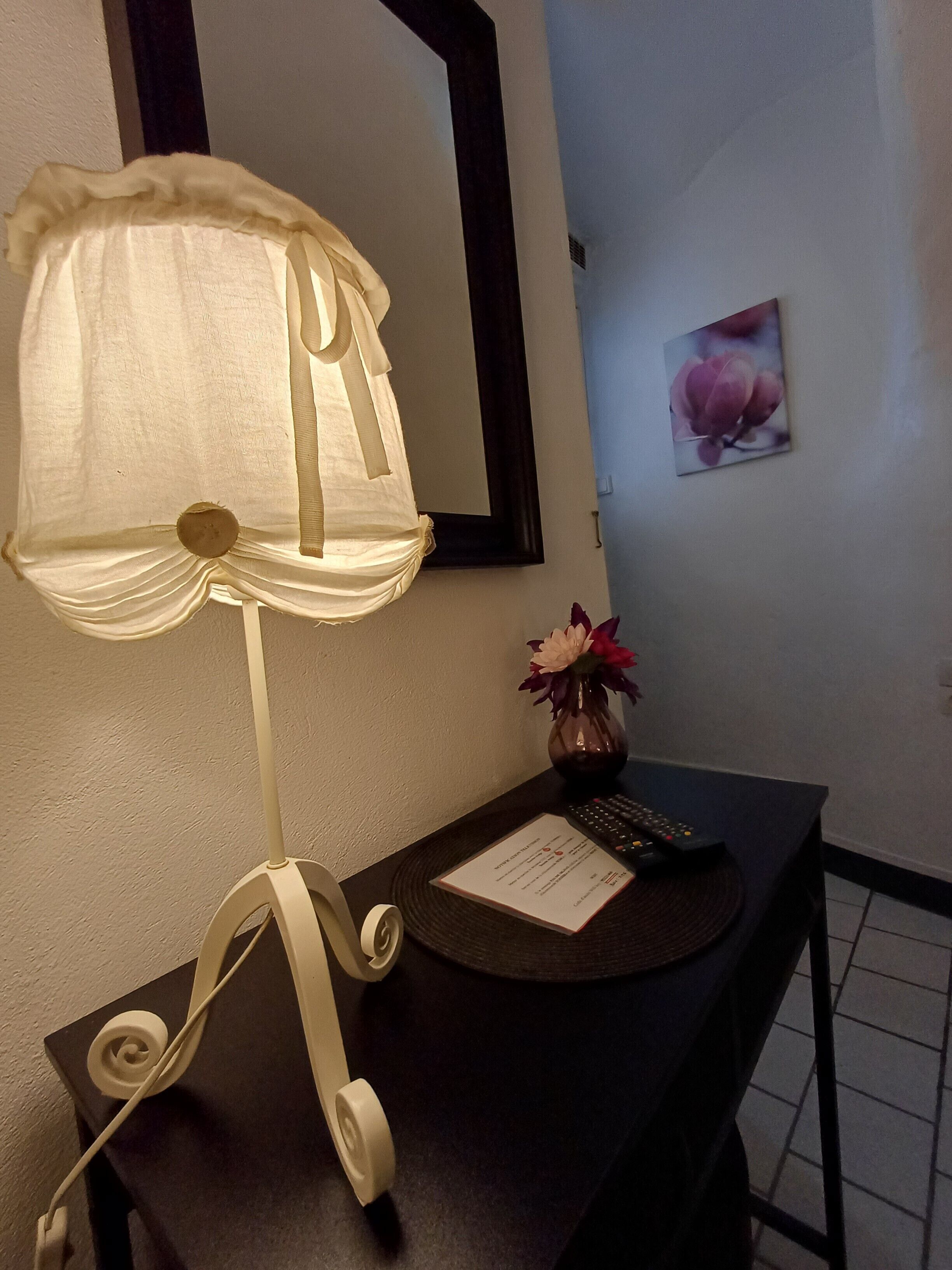 Una habitación con una mesa, una lámpara, un florero con flores, un cuadro enmarcado y un menú.