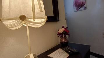 Una habitación con una mesa, una lámpara, un florero con flores, un cuadro enmarcado y un menú.