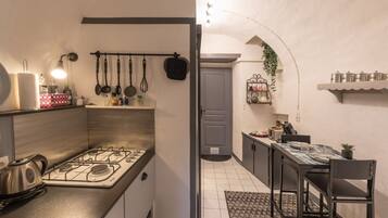 Una cucina compatta con piano cottura a gas, utensili appesi, bollitore e un'area pranzo con tavolo e sedie.