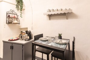 A dining area with a table set for two, a coffee machine, a kettle, and a shelf with jars.