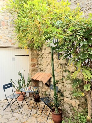 A stone wall, a cactus, a metal table with chairs, and a potted plant.