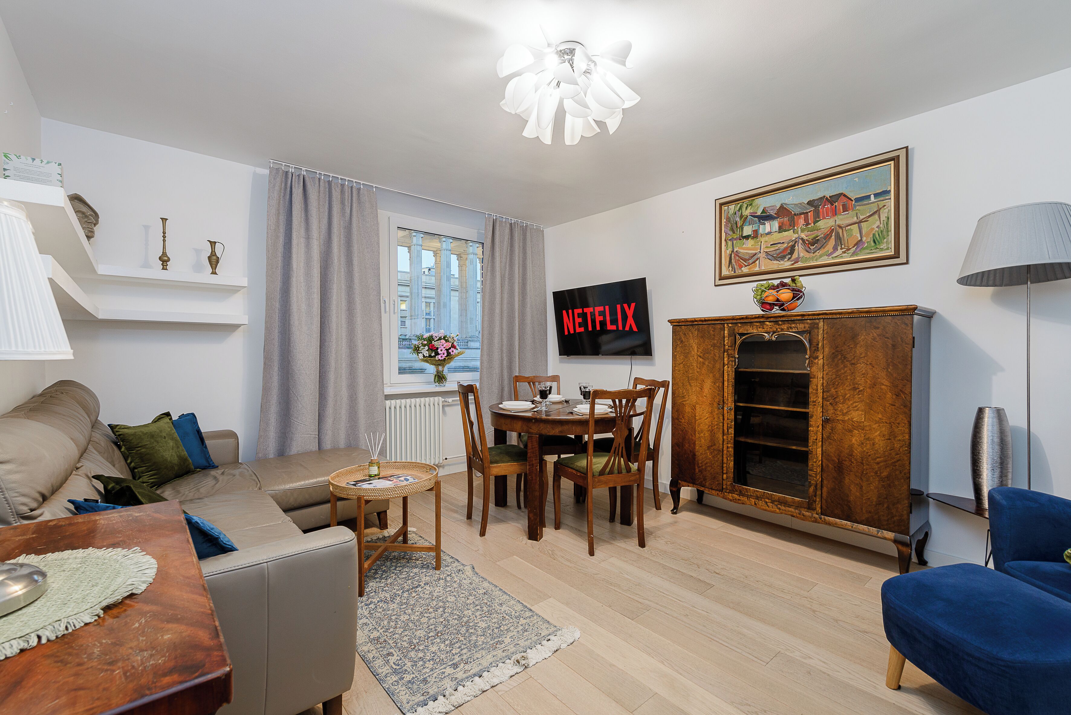 Een woonkamer met een bank, een salontafel, een eettafel met stoelen, een televisie en een kast.