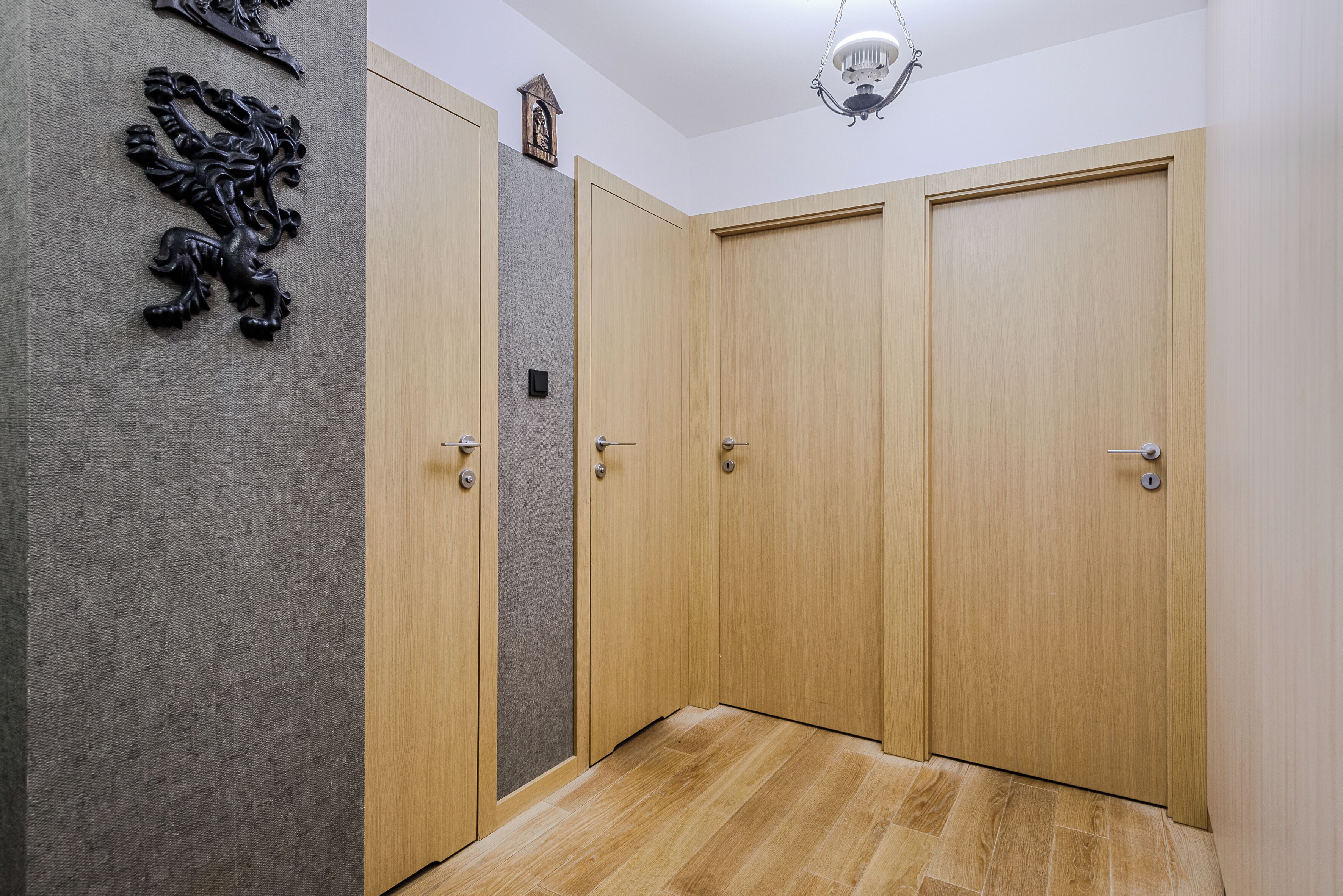A hallway with four wooden doors, a textured wall, and a wooden floor.