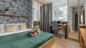A bedroom with a bed, a desk, and a chair. There is a mirror, a plant, and a window. - Lumina apartment in center Warsaw (Warsaw)
