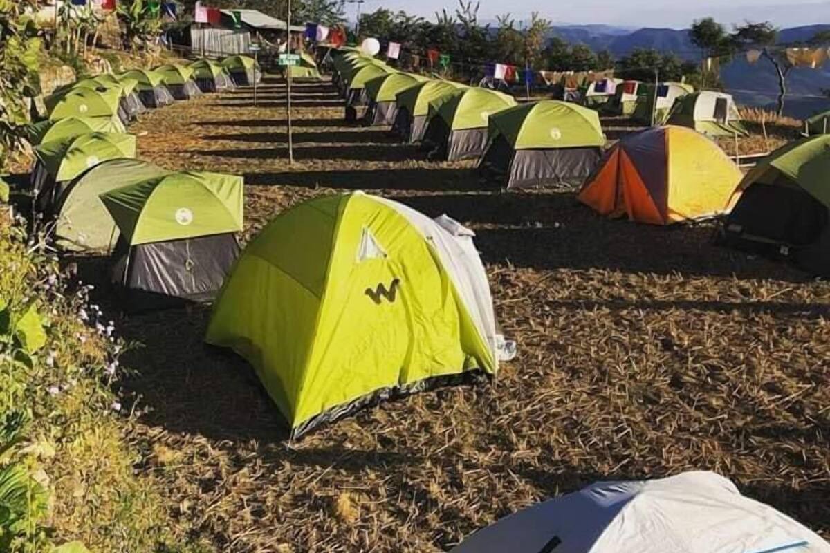 Un terrain de camping avec de nombreuses tentes disposées en rangées, entouré d’un paysage naturel et sous un ciel dégagé.