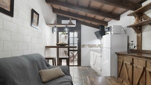 Un espace de vie compact comprenant un canapé, une table en bois, un coin cuisine avec des placards et un four à micro-ondes, ainsi qu’un sol carrelé.