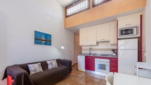 A living room with a sofa, a dining table, and a kitchen with cabinets and appliances.