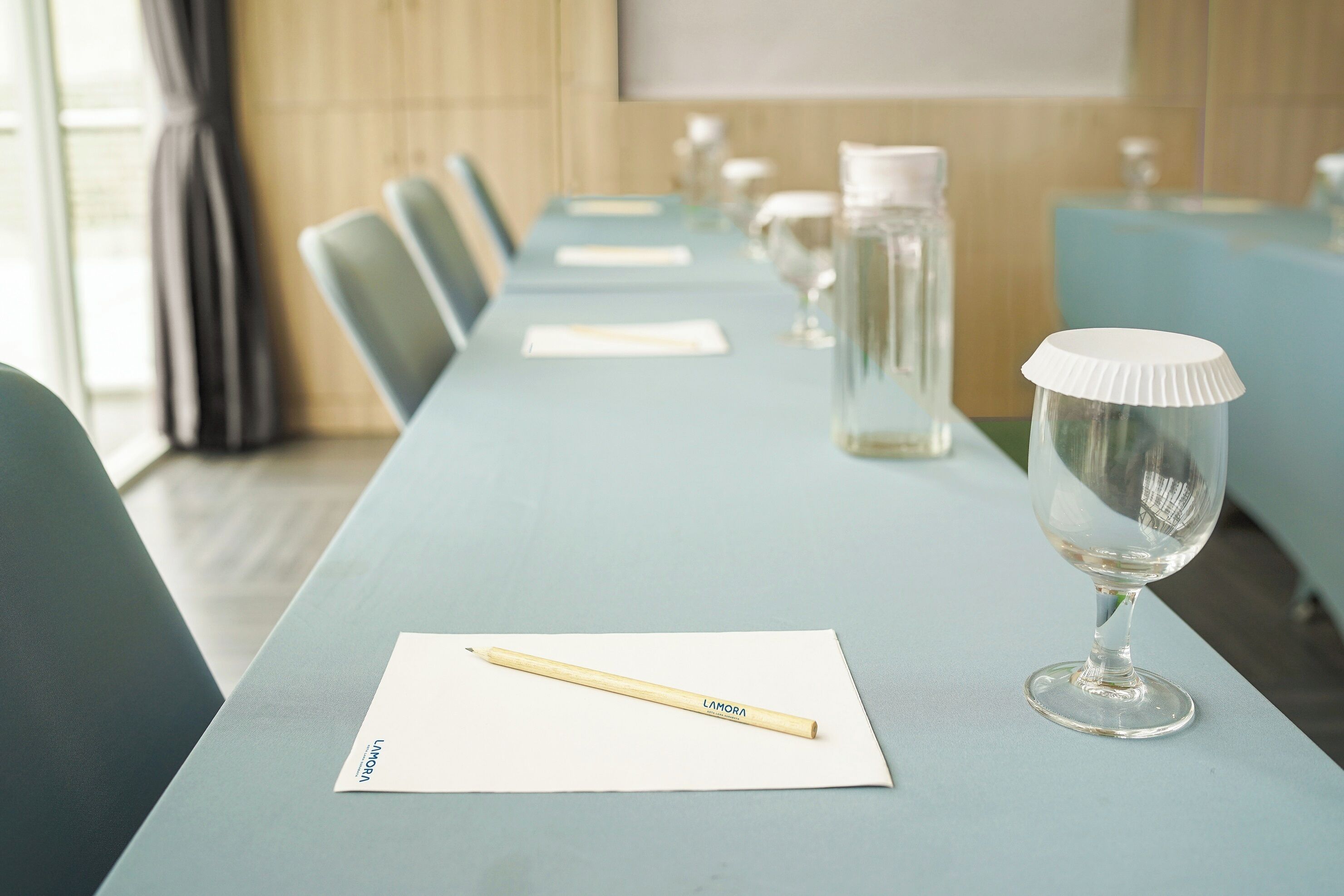 A conference room with a long table, chairs, a glass of water, a bottle, and a pencil on a napkin.
