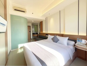 A modern hotel room with a large bed, a bedside table with a coffee maker, and a bathroom with a sink and mirror.