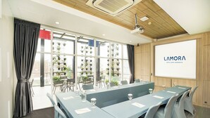 Een vergaderzaal met een lange tafel, stoelen en een projectorscherm waarop 'LAMORA KOTA LAMA SUREBAYA' staat.