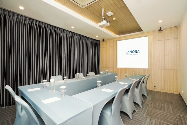 A conference room with a long table, chairs, and a screen displaying "LAMORA".