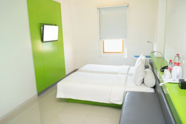 A hotel room with a bed, a bench, a TV, a window, and a bathroom with a sink and toiletries.