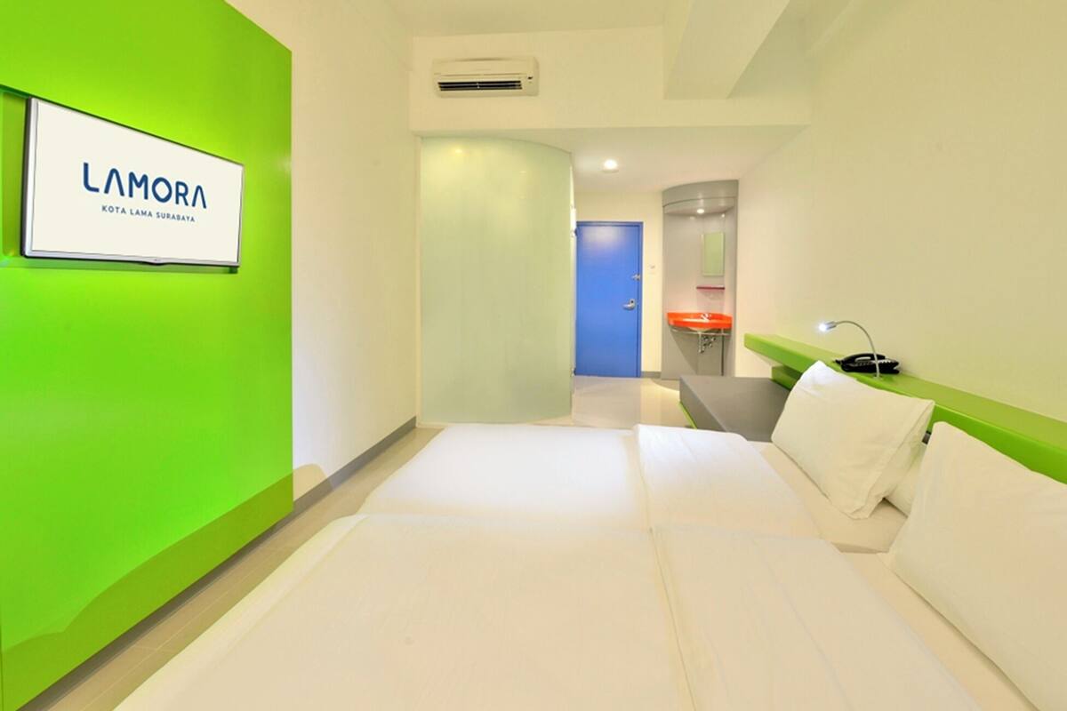 Une chambre d’hôtel avec un lit, une table de chevet, une lampe et une salle de bain visible à travers une porte ouverte.
