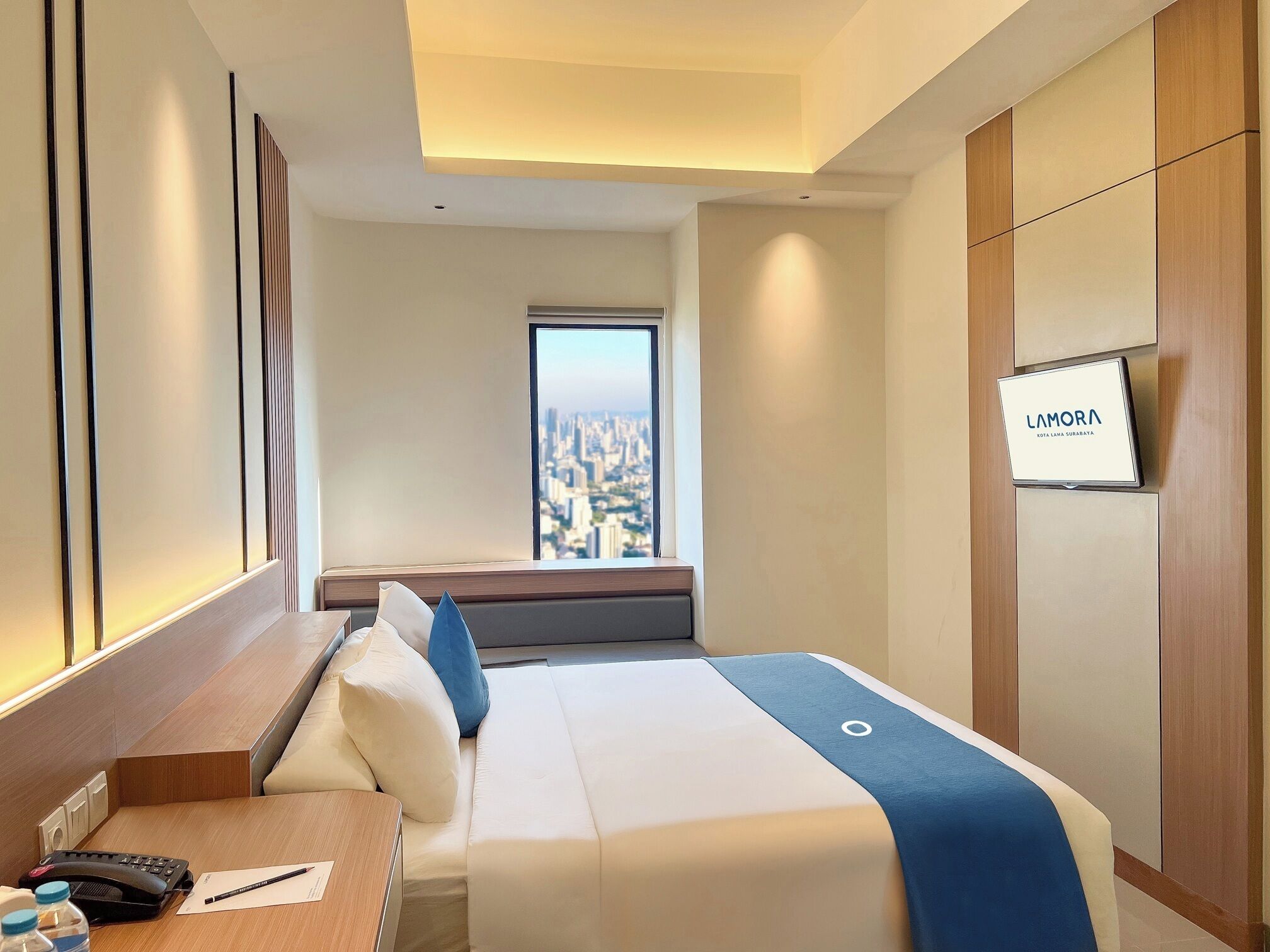 Ein Hotelzimmer mit Bett, Schreibtisch, Telefon und Fenster mit Blick auf die Stadt.