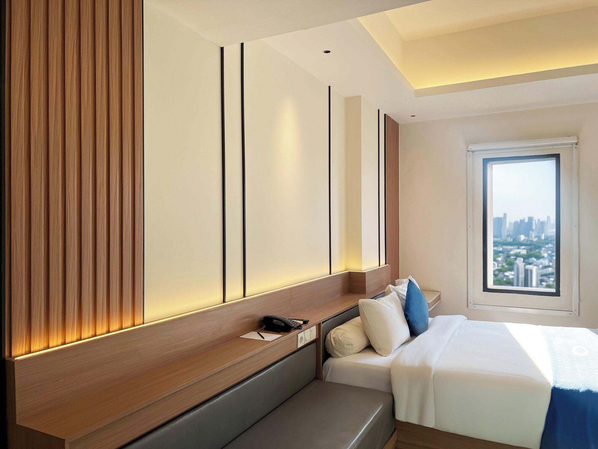 Une chambre d’hôtel moderne avec un grand lit, une table de chevet avec un téléphone et une vue sur la ville par la fenêtre.