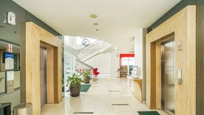 Een moderne hotel lobby met een centrale trap, liften en potplanten.