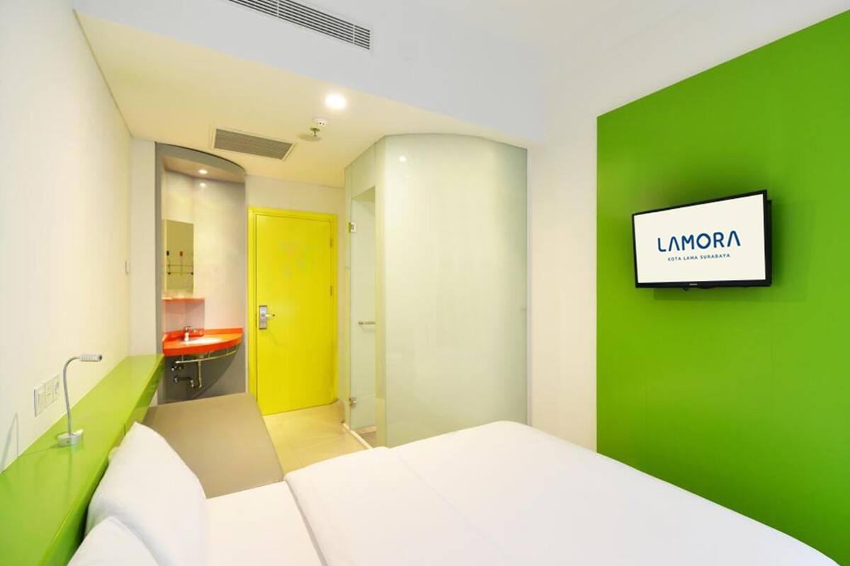 Une chambre d’hôtel avec un lit, un mur d’accent vert, un lavabo et un miroir.
