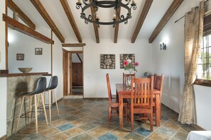 A dining area with a wooden table and chairs, a chandelier, and a stone wall.