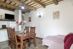Uma sala de jantar com uma mesa de madeira, cadeiras, um vaso com flores, uma garrafa de vinho e uma TV em um armário branco.