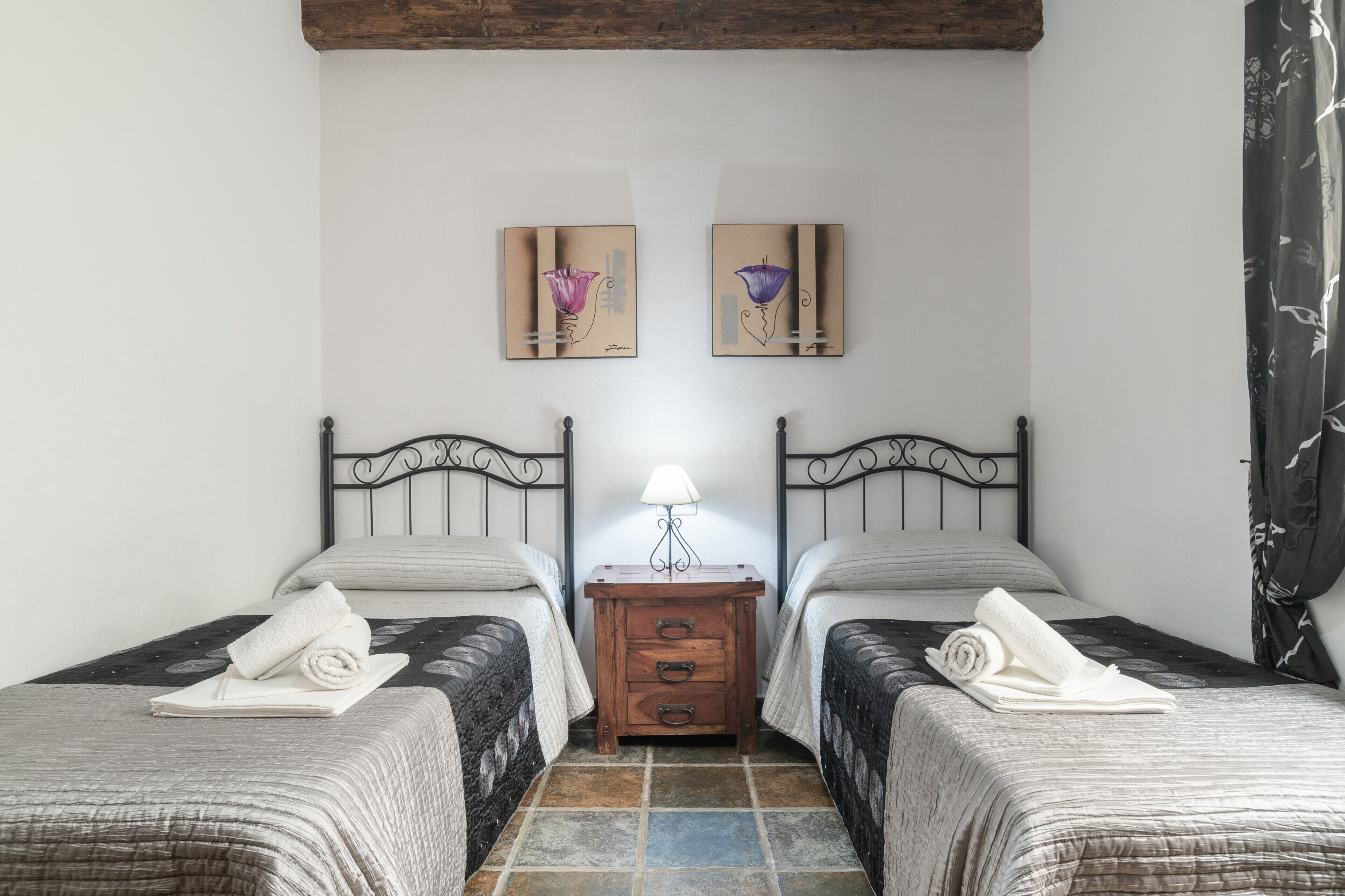 Une chambre avec deux lits, une table de chevet avec une lampe et des œuvres d’art accrochées au mur.