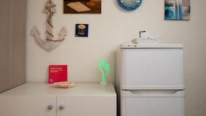 A room with a white cabinet, a refrigerator, and various wall decorations including an anchor, a painting, and a neon cactus. - Mishti Blu Studio al Mare by Wonderful Italy (Olbia)