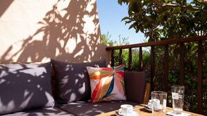 A wooden table with a cup and two glasses, a cushioned bench with a colorful pillow, and a railing with greenery in the background. - Mishti Blu Studio al Mare by Wonderful Italy (Olbia)