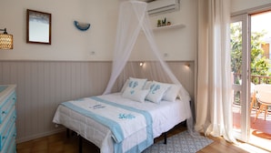 A bedroom with a bed, a bedside table, a dresser, a window with curtains, and an air conditioning unit. - Mishti Blu Studio al Mare by Wonderful Italy (Olbia)