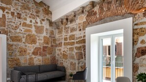 A room with exposed stone walls, a grey sofa, a small table, and a chair. - Casa di Design tra le Mura by Wonderful Italy (Palermo)