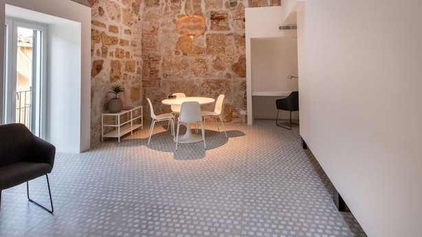 A modern interior with a stone wall, a round table with chairs, a black chair, and a white ceiling with skylights. - Casa di Design tra le Mura by Wonderful Italy (Palermo)
