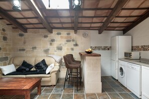 A cozy kitchen with a stone wall, a wooden ceiling, a washing machine, and a microwave.