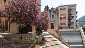 Un edificio con una scala in pietra che conduce a un balcone, circondato da piante e fiori in vaso.
