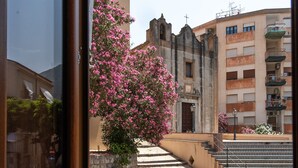Vista attraverso una finestra di un edificio con una scala in pietra che conduce a una piazza, un albero in fiore rosa e una chiesa con una croce.