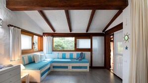 Una habitación acogedora con un banco empotrado, vigas de madera, un aparador blanco y una ventana con cortinas.