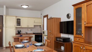 A compact kitchen with wooden cabinets, a dining table set for four, a microwave, and a television.