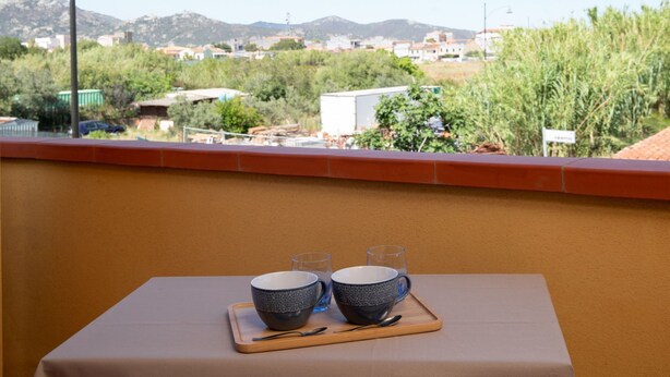 A balcony with a table set for two, overlooking a scenic landscape with mountains and greenery.