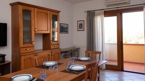 A dining area with a wooden table set for two, a cabinet with glass doors, and a view of the outside through a sliding glass door.