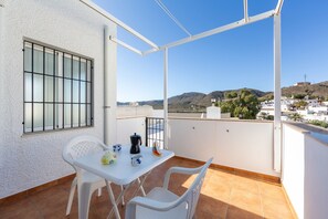 A balcony with a white table, chairs, and a window with bars.